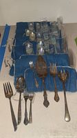 Multiple flatware pieces and serving utensils laid out in blue roll