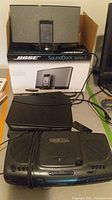 Photo showing Bose SoundDock Series II music system on top of box, digital CD player, black device case and cables on table.