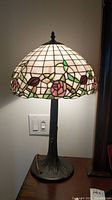 Front view of the stained glass lamp showing the floral rose stained glass shade and textured tree trunk style base.