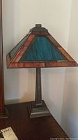 Full view of the stained glass lamp showing the triangular blue and brown panels of the shade and the metal base on a flat surface.
