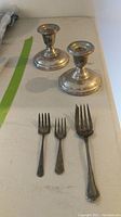 Two weighted sterling silver candlesticks and three sterling silver forks (one salad fork, two hors d'oeuvre forks) displayed on a surface, showing overall shape and tarnish condition.