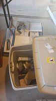 View showing a closed gray plastic bin with a variety of home repair items visible inside, along with a large box beneath it.