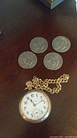 Four 1977 Eisenhower silver dollars arranged above gold-tone pocket watch and chain
