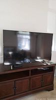 Front view of the 55 inch TCL Roku TV on wooden media console.