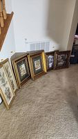 Six framed wall art pieces leaning against wall on carpet, showing all items in the lot.