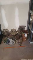 Three carved wall decor pieces, two shelves, large decorative vase, and bag of decorative stones arranged on floor against wall.