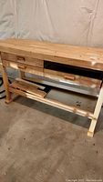 Front and angled front views of the wooden worktable showing three drawers with wooden handles, one drawer detached and resting on the bottom shelf, and the solid wooden work surface