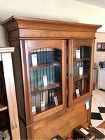 Front view of antique wooden bookcase with glass doors filled with books and a closed pull-down desk door below.