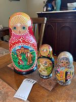 Photo shows three large nesting dolls from the larger set with detailed painting and a ticket in the foreground.