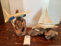 Both ocean-themed sculptures shown side by side on a reddish-brown patterned surface with white wall background. The shark sculpture positioned left, sailboat positioned right.