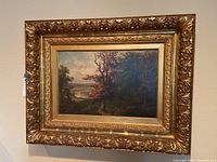 Full view of landscape painting in ornate gold-tone carved wooden frame