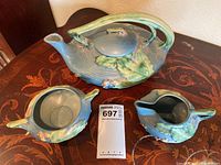 Full set image showing teapot, sugar dish, and creamer on wooden table with visible glaze colors and design
