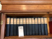 Full set of 13 black cloth hardcover books by Charles Reade with cream-colored spine labels in wooden bookcase