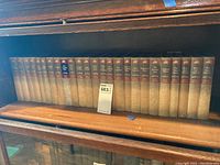 Full shelf view of 24 Max Brand hardcover books lined up on a wood shelf, showing beige cloth spines with brown-red labels and a horse rider emblem