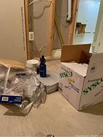 photo showing items on basement floor including plastic cups, paper plates in box, a silver case, and a blue water bottle