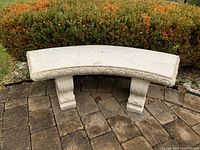 Front view of curved concrete bench on patio showing decorative carved legs and circular motif along front edge.