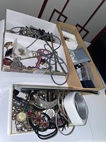 Two boxes containing a variety of mixed metal and rhinestone costume jewelry including bracelets, necklaces, rings, brooches in assorted styles and colors.