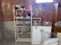 Wide view of the craft supplies organized on a white metal shelving unit and adjacent boxes in a basement setting with unfinished walls.