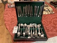 Wide angle view of entire cutlery set inside wooden box with green felt lining showing knives in slots on lid and other cutlery in the base section.