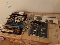 Top view showing a wooden box and blue basket containing assorted metal kitchen utensils including spoons, forks, knives, and various servers plus other kitchen tools.