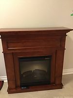 Front view of electric fireplace showing wooden mantel and glass front with simulated logs.