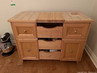 Front view of wooden kitchen island showing tile top with cutting board, drawers and cabinet doors.