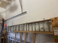 Side view showing full length of aluminum extension ladder mounted on wall alongside wooden ladder