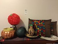 Overview of lamp with red spherical shade, Greek vase, cushions, decorative balls, and plates