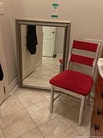 Photo showing the wood framed mirror leaning against wall and red upholstered wooden chair with chipped/faded paint.