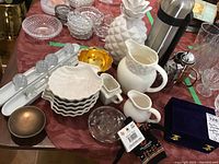 Main table view showing pitchers, shell bowls stacked, decorative ceramic pineapple, coffee thermos, napkin rings, brass bowl, flower frog and other kitchen/dining items.