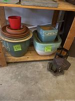 Shelf with various ceramic and plastic planters stacked alongside metal bird feeder.