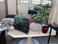 Overview of lot items on round white table showing LED gift box, faux plant, twig pumpkin and metal planter