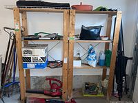 Two wooden shelving units in a garage environment with various tools and items on the shelves. Shelves have a natural wood finish and show signs of light use.