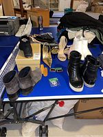 Overall view of the lot on a blue table showing multiple shoes, boots, bags and shoe accessories.