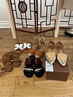 Five pairs of women's shoes and sandals arranged on floor, showing various styles and colors.