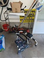 Photo showing two wooden hockey sticks leaning against a wall near a metal rack, a blue inline roller blade placed on the floor, a black and white exerciser, and deflated balls in the background.