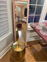 Photo showing the gold-colored metallic stand beside the wood-framed mirror, highlighting the stand's shiny finish and the mirror's height and frame color.