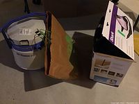 Photo of Bissell PowerLifter steam cleaner, brown paper bag, and boxed Shark steam cleaner on floor