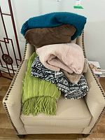 View of entire stack of eight assorted throws on cream studded armchair, showing variety in color and texture