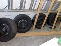 Four black Semperit tires on black steel rims lined up inside a garage, resting on the floor against a wall.