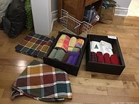 Two wooden boxes with assorted towels, including Christmas themed, next to folded plaid placemats on floor