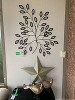 Photo of the metal star and black tree branch wall art hung on a wall with two wooden bird figurines in front on a black surface.