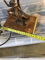 Close-up of cowboy riding horse figurine on copper rectangular base with measuring tape showing approx. 20 cm width.