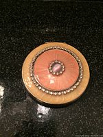 Top view of round compact mirror with pink and cream enamel and clear stones around center stone.