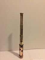 Full view of the antique brass nautical spyglass telescope in extended position showing single barrel and worn cover on bottom section.