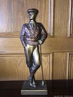 Full front view of the bronze and copper colored golfer sculpture showing detailed argyle sweater, flat cap and golf club.