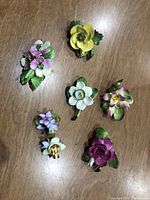 All five bone china flower brooches displayed on wooden surface to show overall lot contents.