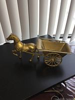 Brass horse pulling a brass cart with spoked wheels on a black surface, side view.