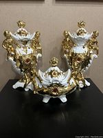 Front view of the set of three Italian porcelain cherub decor pieces on a black surface.