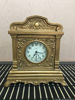 Front view of mid century mantle clock showing ornate gold-tone metal detailing and clock face with Arabic numerals and subdial.